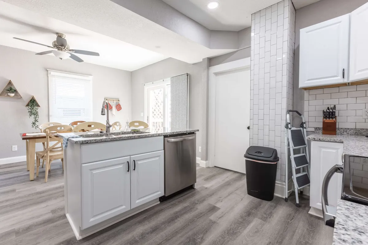 A seamless kitchen and dining area featuring a granite countertop, stainless steel appliances, and a dining table positioned by a window letting in abundant natural light. The setting encourages both cooking and casual family dining.