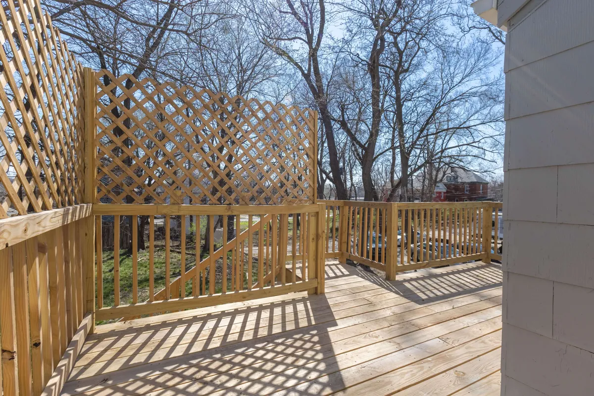 This image features a tranquil wooden deck bordered by a lattice fence, with mature trees creating a peaceful, leafy backdrop. The setting is ideal for outdoor gatherings, relaxation, and family barbecues, with a sense of privacy and connection to nature.