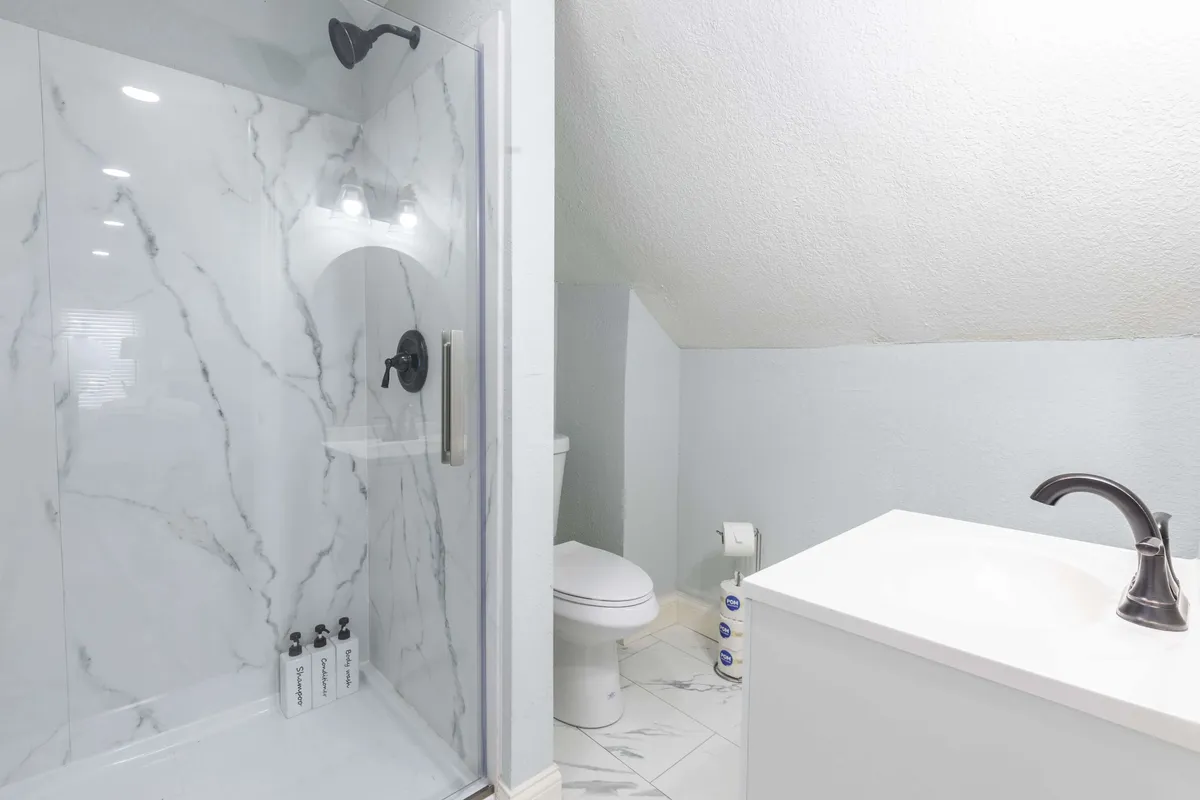A modern bathroom featuring a shower with a clear glass door, marble tile, and a sleek sink with a contemporary faucet. The clean lines and bright lighting create a fresh, tranquil atmosphere perfect for unwinding.
