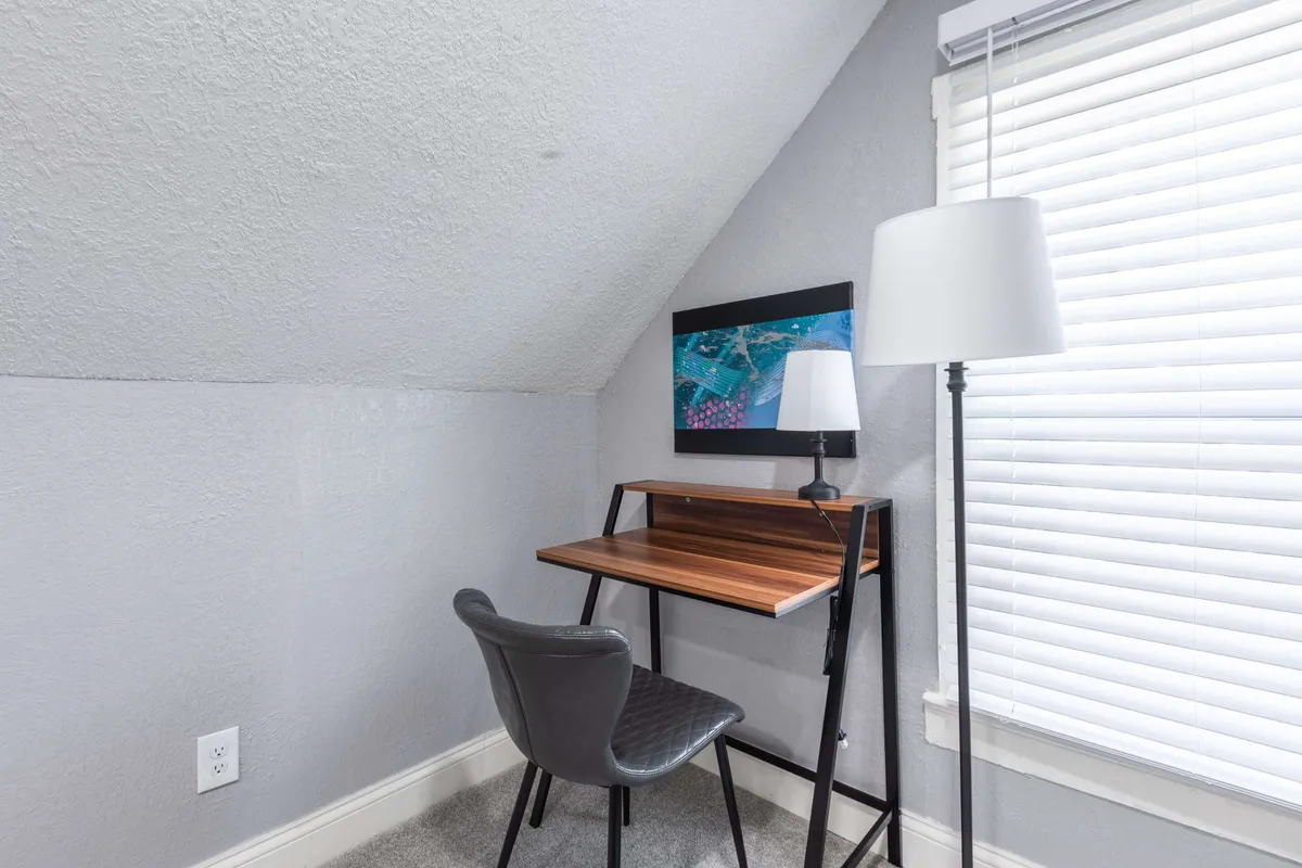 A cozy workspace featuring a desk, comfortable chair, lamp, and inspiring artwork. The serene setup is ideal for focused work, study sessions, or quiet calls, providing a sense of productivity and calm.