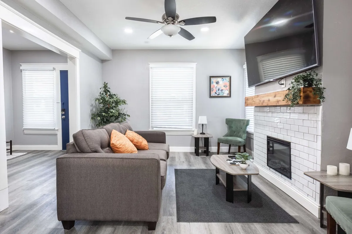 A comfortable living area with a sofa adorned with orange cushions, a coffee table, a fireplace, a television, and a green chair. The furniture is arranged for conversation and relaxation, set against a backdrop of modern decor and new flooring.