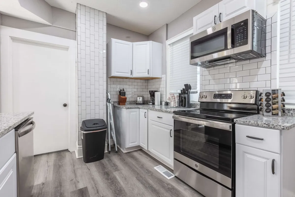 A contemporary kitchen featuring stainless steel appliances, white cabinetry, granite countertops, and a modern backsplash. The space is open and inviting, exuding an atmosphere perfect for both cooking and gathering. It’s well-lit and showcases ample counter space for meal prep and entertaining.