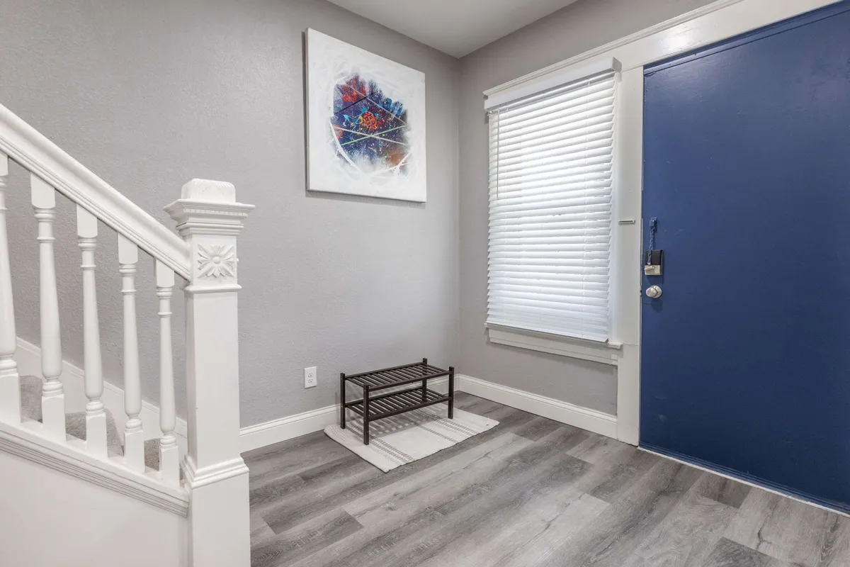 This inviting entryway showcases a stylish blue front door, contemporary abstract wall art, and a staircase leading up, creating a warm first impression. The scene hints at a welcoming home base for families to start and end their city explorations.
