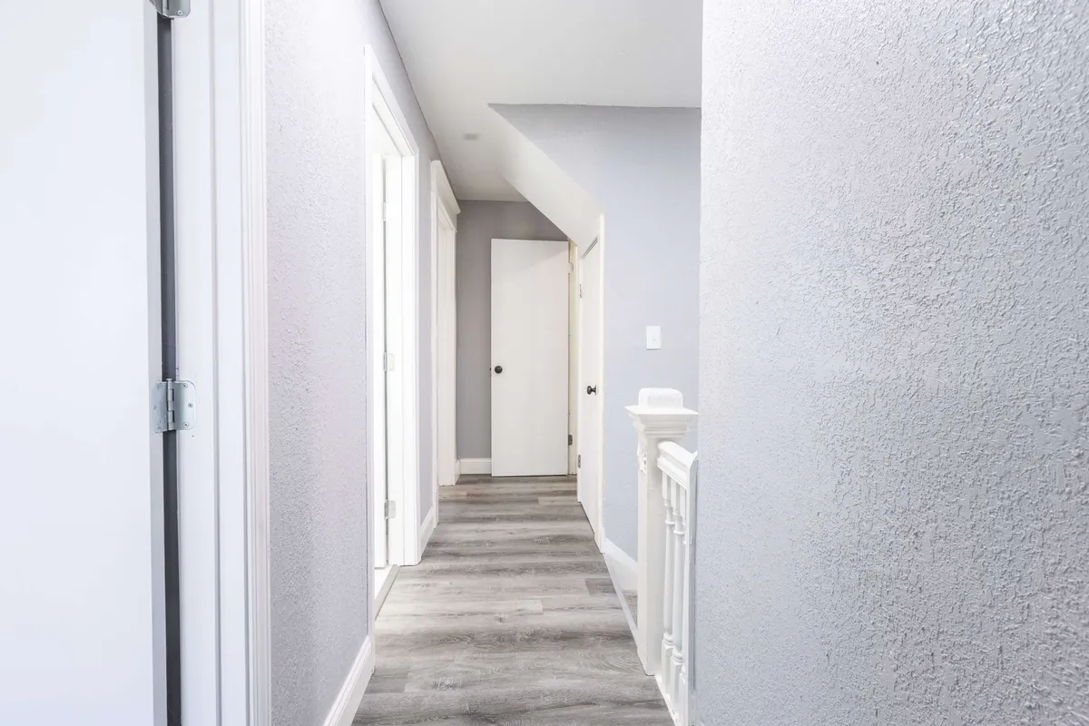 A long, airy hallway lined with doors and ending with an open railing, creating a sense of flow and connectivity throughout the home. The bright, inviting atmosphere encourages movement and interaction among guests.