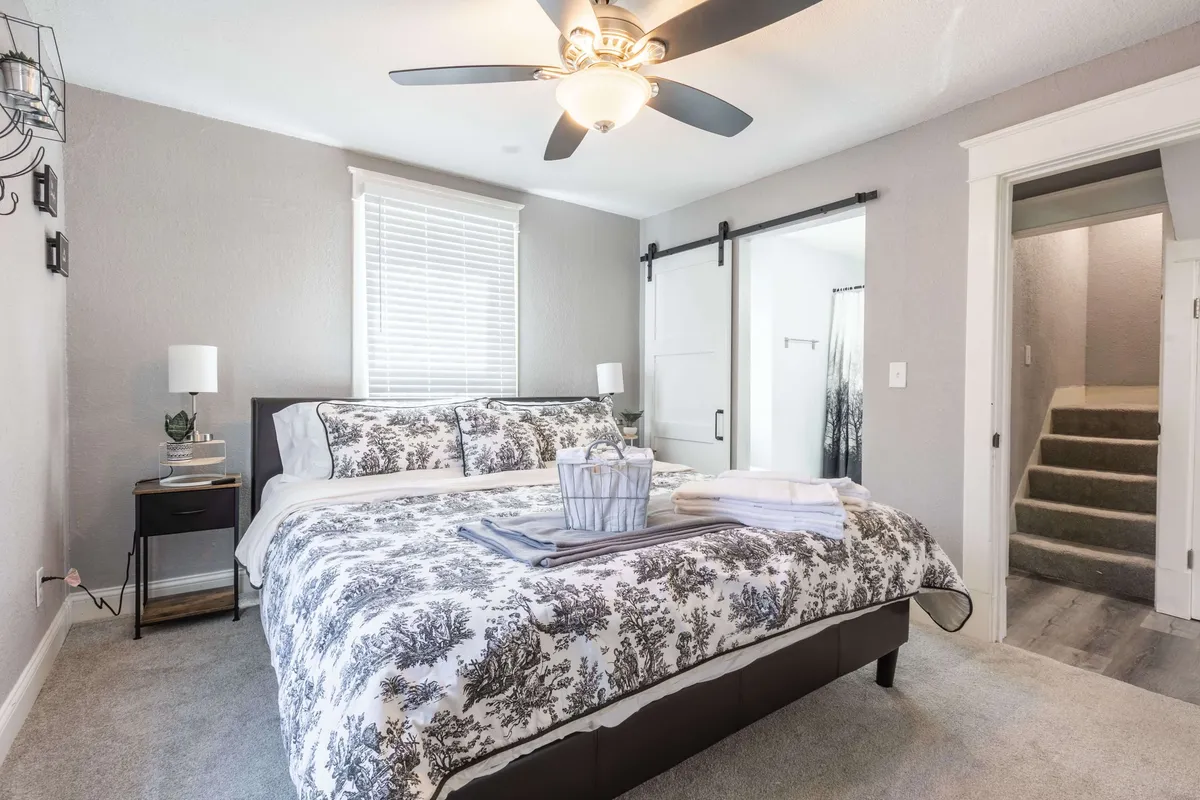 A tranquil bedroom featuring a bed with decorative bedding, a cozy nightstand with a lamp, and a sliding barn door. Soft natural light filters in through the window, creating a calm and inviting space perfect for resting or reading.